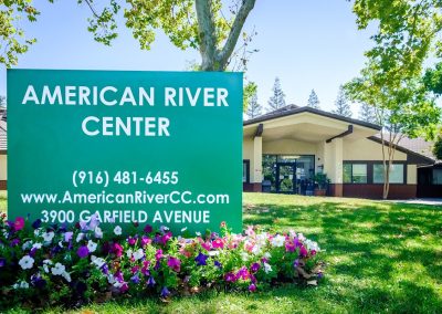 The front of the American River Center showing the monument sign, green grass and trees.
